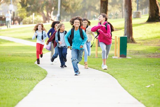 A diverse group of smiling children wearing backpacks running along a pathway.